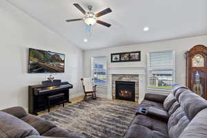 Living room featuring ceiling fan, a stone fireplace, lofted ceiling, and hardwood / wood-style floors