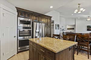 Kitchen featuring a center island, stainless steel appliances, light wood-type flooring, pendant lighting, and ceiling fan with notable chandelier