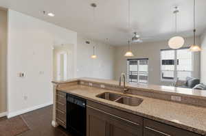 Kitchen featuring dishwasher, decorative light fixtures, light stone countertops, and sink