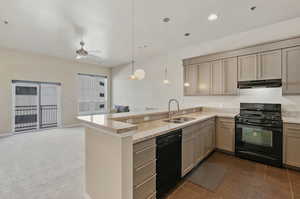 Kitchen with dark colored carpet, kitchen peninsula, black appliances, sink, and pendant lighting