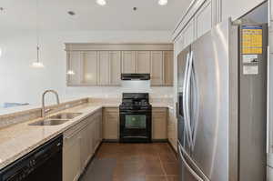 Kitchen with black appliances, light stone countertops, hanging light fixtures, sink, and kitchen peninsula