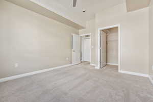 Unfurnished bedroom featuring ornamental molding, ceiling fan, a walk in closet, light colored carpet, and a closet