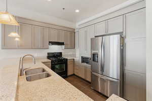 Kitchen featuring dark tile patterned flooring, light stone counters, hanging light fixtures, sink, and appliances with stainless steel finishes