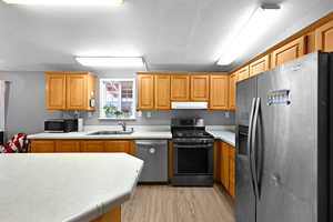 Kitchen with light wood-type flooring, appliances with stainless steel finishes, a textured ceiling, and sink