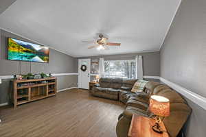 Living room with lofted ceiling, hardwood / wood-style floors, ceiling fan, and crown molding