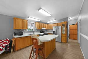 Kitchen with stainless steel appliances, light hardwood / wood-style floors, a center island, sink, and a kitchen breakfast bar