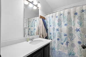 Bathroom featuring vanity, curtained shower, and vaulted ceiling