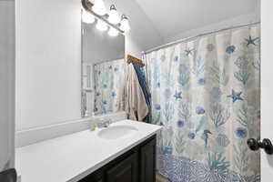 Bathroom featuring walk in shower, vanity, and vaulted ceiling