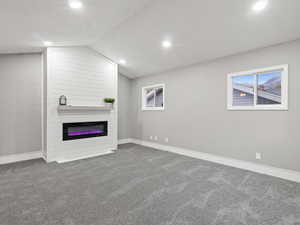 Unfurnished living room featuring a large fireplace, vaulted ceiling, and carpet