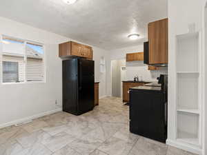 Kitchen featuring a textured ceiling, black fridge, sink, and electric range