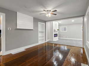 Living room with ceiling fan, a textured ceiling, a large fireplace, wood-type flooring, and built in features