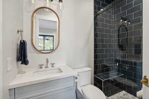 Bathroom featuring toilet, vanity, and tiled shower