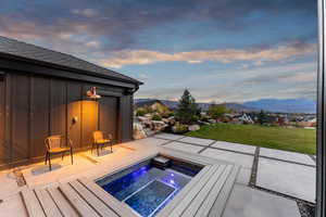 Pool at dusk featuring a patio, a mountain view, a yard, and a hot tub