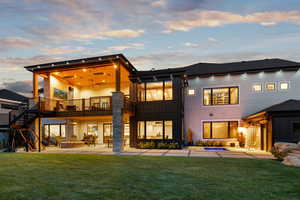 Back house at dusk with a lawn, a balcony, a jacuzzi, and a patio area