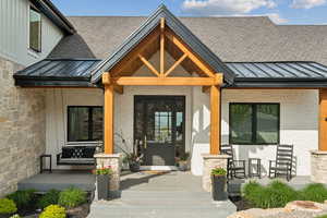 Entrance to property featuring covered porch, a standing seam roof, a shingled roof, and brick siding