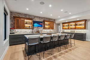 Bar with light wood-type flooring, decorative backsplash, and brick wall