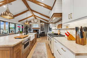 Kitchen featuring a brick fireplace, a large island with sink, white cabinetry, and decorative light fixtures