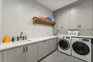 Washroom featuring cabinets, light tile patterned floors, sink, and washing machine and clothes dryer