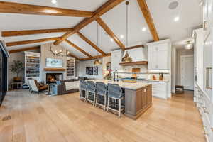 Kitchen with white cabinets, a large island, beam ceiling, pendant lighting, and light wood-type flooring