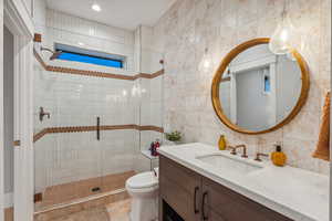 Bathroom with tile walls, tile patterned floors, a shower with door, vanity, and toilet