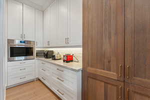 Kitchen with white cabinetry, light hardwood / wood-style flooring, light stone counters, and stainless steel oven