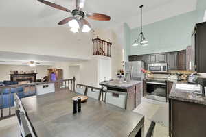 Tiled dining area with ceiling fan with notable chandelier, sink, and high vaulted ceiling