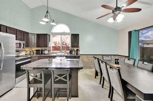 Kitchen featuring dark brown cabinetry, appliances with stainless steel finishes, a breakfast bar area, a center island, and pendant lighting