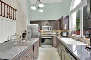 Kitchen with stainless steel appliances, sink, light tile patterned floors, hanging light fixtures, and a towering ceiling