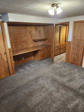 Unfurnished bedroom with wooden walls, carpet floors, and ceiling fan