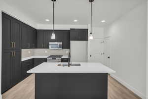 Kitchen featuring appliances with stainless steel finishes, decorative light fixtures, sink, an island with sink, and light hardwood / wood-style floors