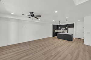 Kitchen with a center island with sink, pendant lighting, ceiling fan, and light hardwood / wood-style floors