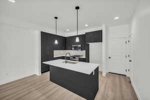 Kitchen featuring light wood-type flooring, appliances with stainless steel finishes, pendant lighting, decorative backsplash, and sink