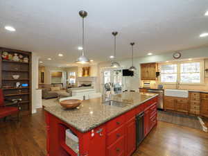 Kitchen with dark wood-type flooring, light stone countertops, sink, and a center island with sink