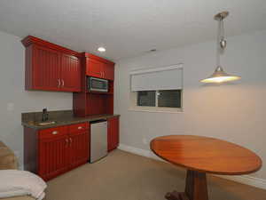 Kitchen with appliances with stainless steel finishes, hanging light fixtures, a textured ceiling, and light colored carpet