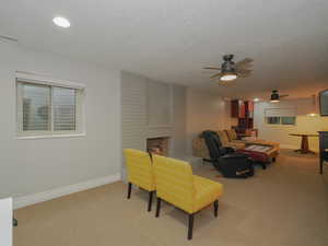 Carpeted living room featuring a brick fireplace, a textured ceiling, and ceiling fan