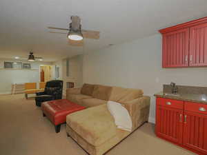 Carpeted living room with a brick fireplace, ceiling fan, a textured ceiling, and sink