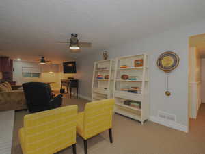 Carpeted living room with ceiling fan and a textured ceiling