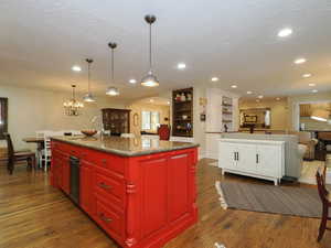 Kitchen with sink, a textured ceiling, a kitchen island with sink, a notable chandelier, and dark hardwood / wood-style flooring