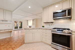 Kitchen featuring decorative backsplash, cream cabinets, and appliances with stainless steel finishes