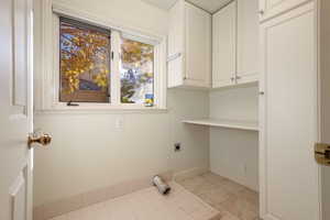 Clothes washing area featuring cabinets, electric dryer hookup, and light tile patterned floors