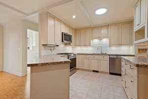 Kitchen with sink, kitchen peninsula, appliances with stainless steel finishes, cream cabinetry, and decorative backsplash