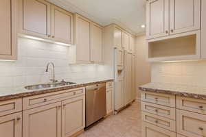 Kitchen with cream cabinets, light stone counters, decorative backsplash, sink, and dishwasher