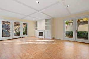 Unfurnished living room with french doors, a wealth of natural light, and coffered ceiling