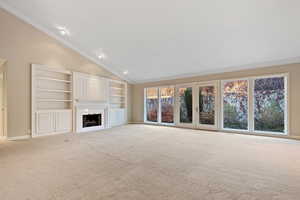 Unfurnished living room with high vaulted ceiling, light colored carpet, and ornamental molding