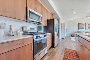 Kitchen with appliances with stainless steel finishes, tasteful backsplash, ceiling fan, a textured ceiling, and light wood-type flooring