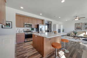 Kitchen with a kitchen bar, stainless steel appliances, a center island with sink, hardwood / wood-style floors, and a textured ceiling