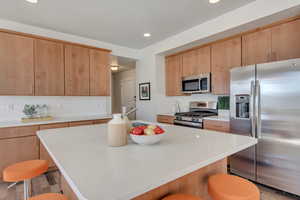 Kitchen featuring decorative backsplash, appliances with stainless steel finishes, a breakfast bar area, and a center island