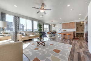 Living room with ceiling fan with notable chandelier, light hardwood / wood-style flooring, and a textured ceiling