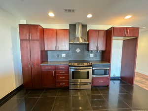 Kitchen featuring tasteful backsplash, dark tile patterned flooring, appliances with stainless steel finishes, and wall chimney exhaust hood