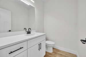 Half bath with baseboards, wood finished floors, vanity, and toilet